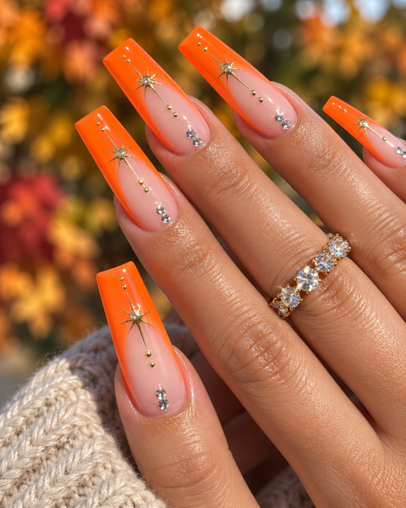 Neon orange Halloween coffin nails with rhinestones and gold starburst details