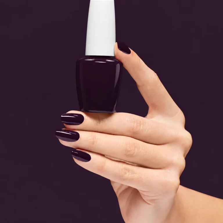 Hand with glossy deep purple nails holding a matching nail polish bottle